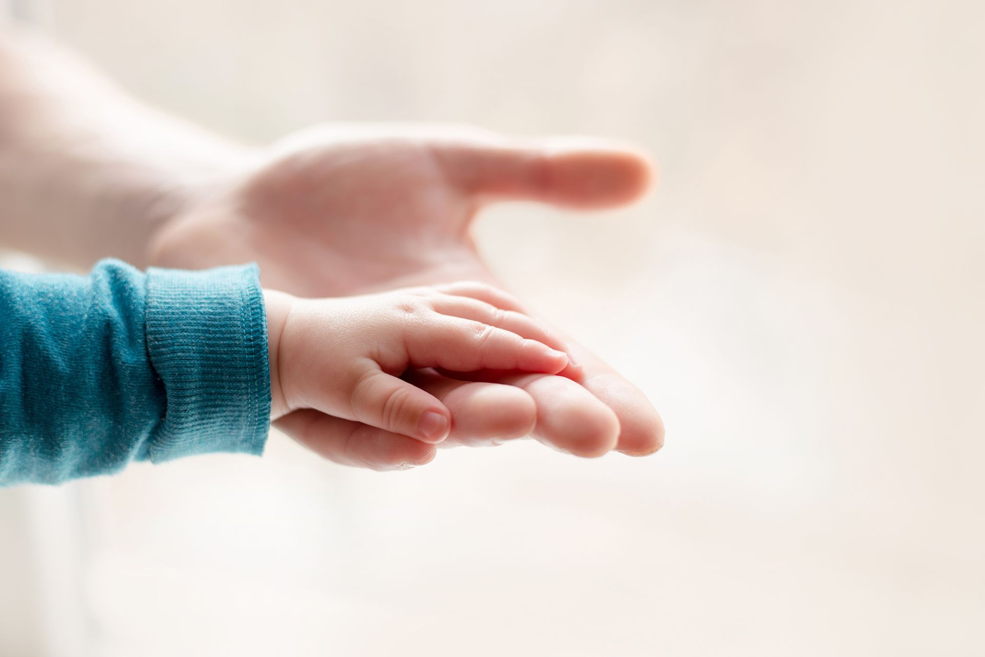 A baby is holding a man 's hand.