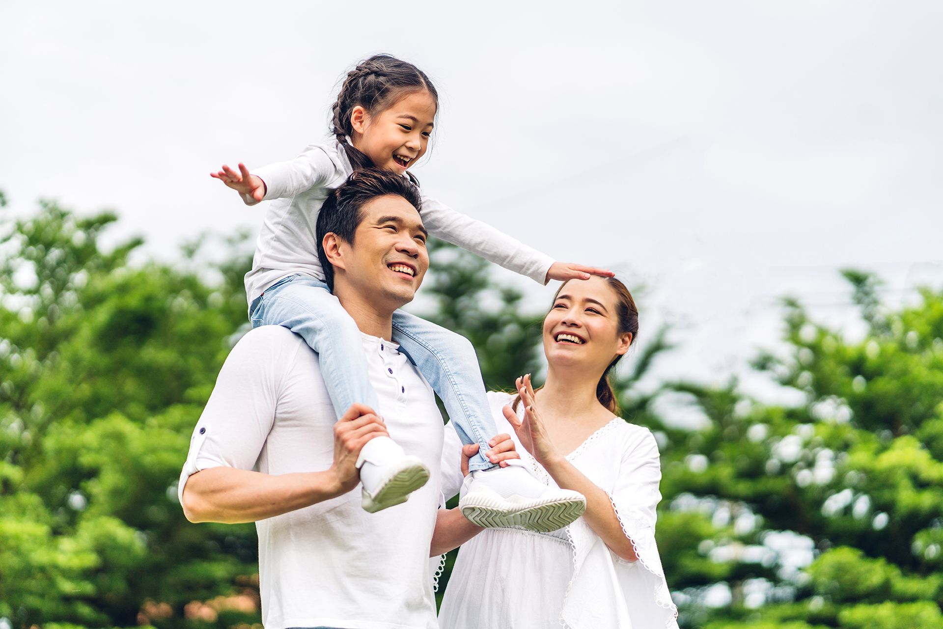 A man is carrying a little girl on his shoulders in a park.