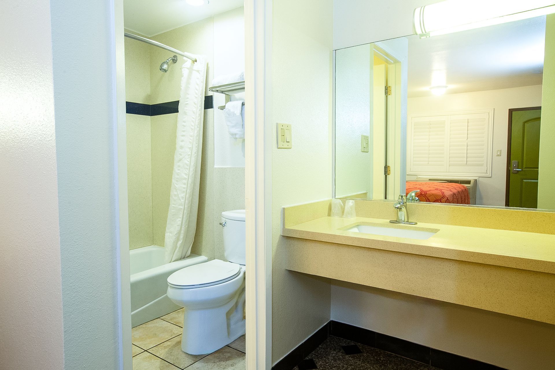 Bathroom with toilet, sink, and shower; neutral colors, simple layout, motel setting.
