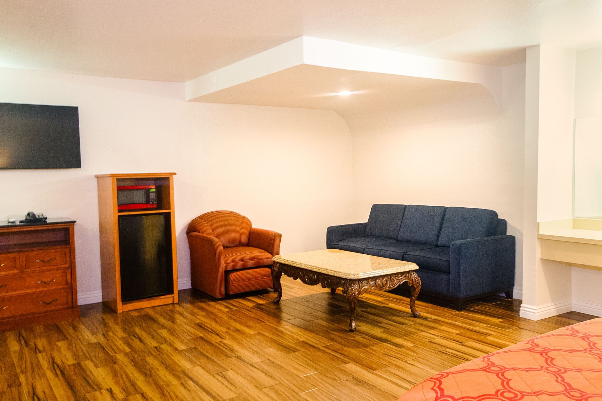 Hotel room with a blue sofa, orange armchair, coffee table, TV, and mini-fridge.