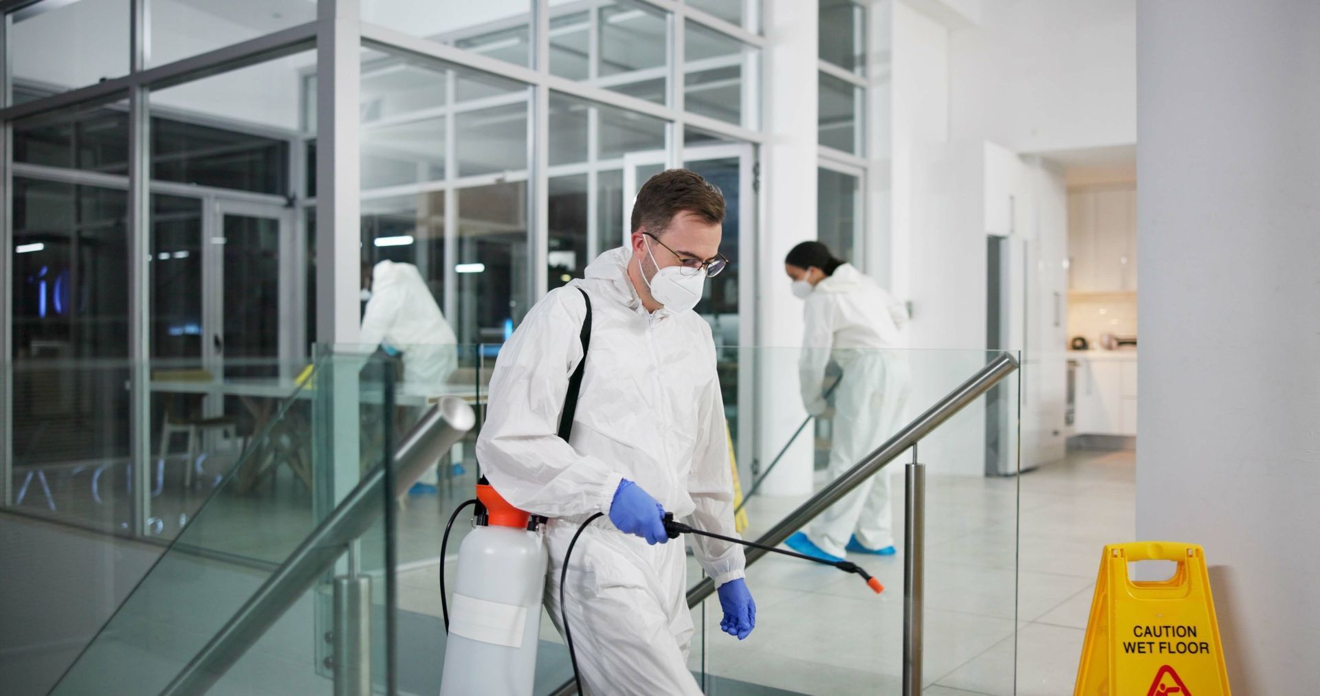 A man in a protective suit is cleaning a building with a sprayer.