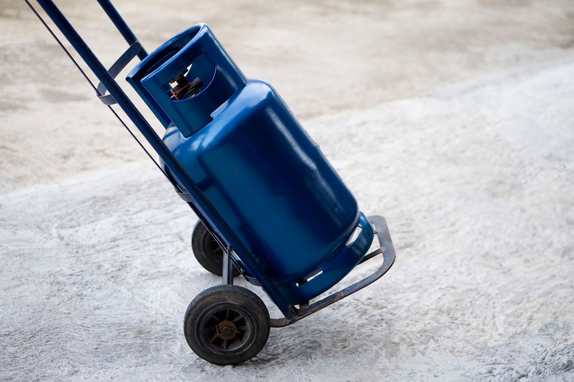 Blue gas cylinder on a hand truck, tilted on a concrete surface