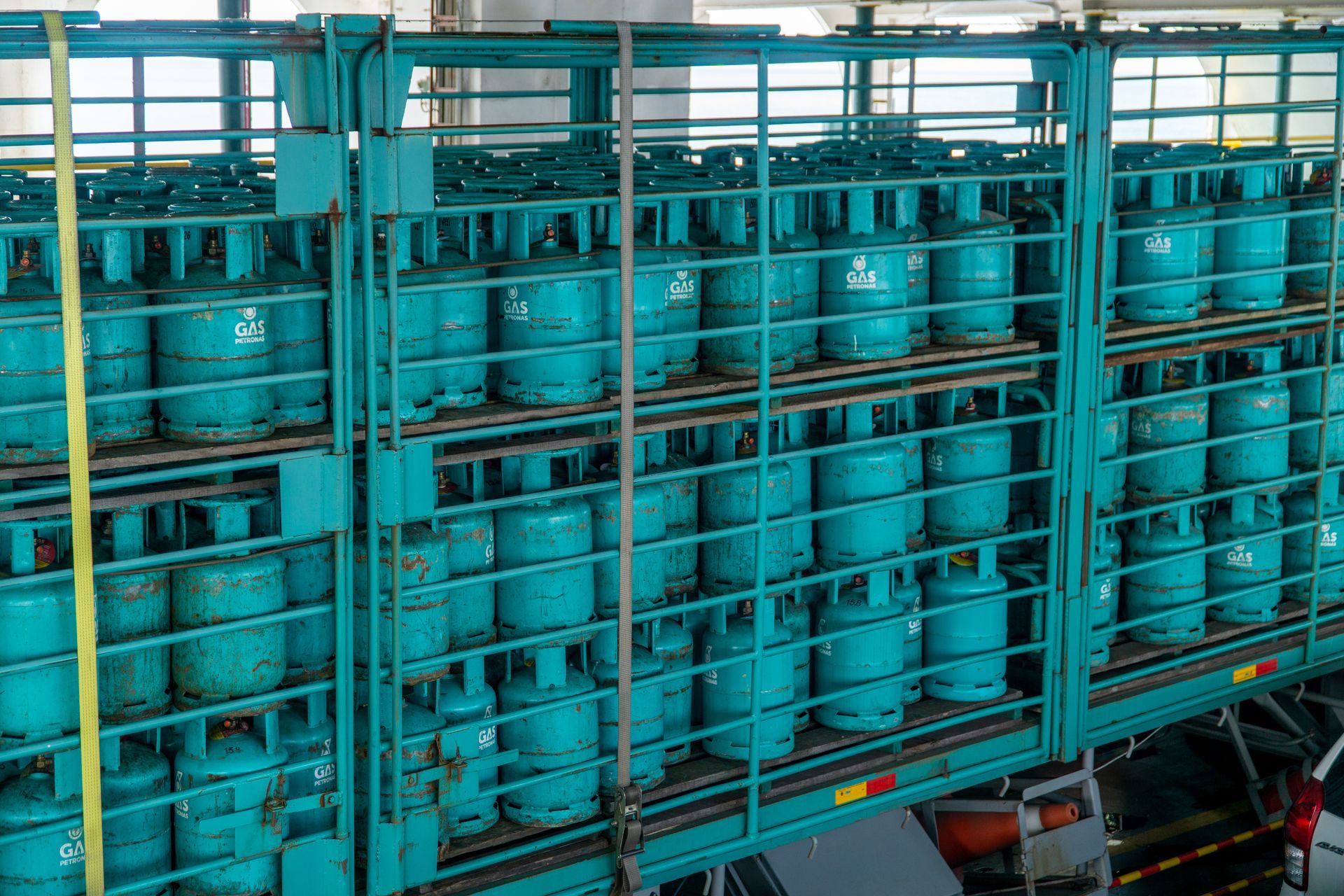 Rows of blue gas cylinders stacked in a metal rack outdoors