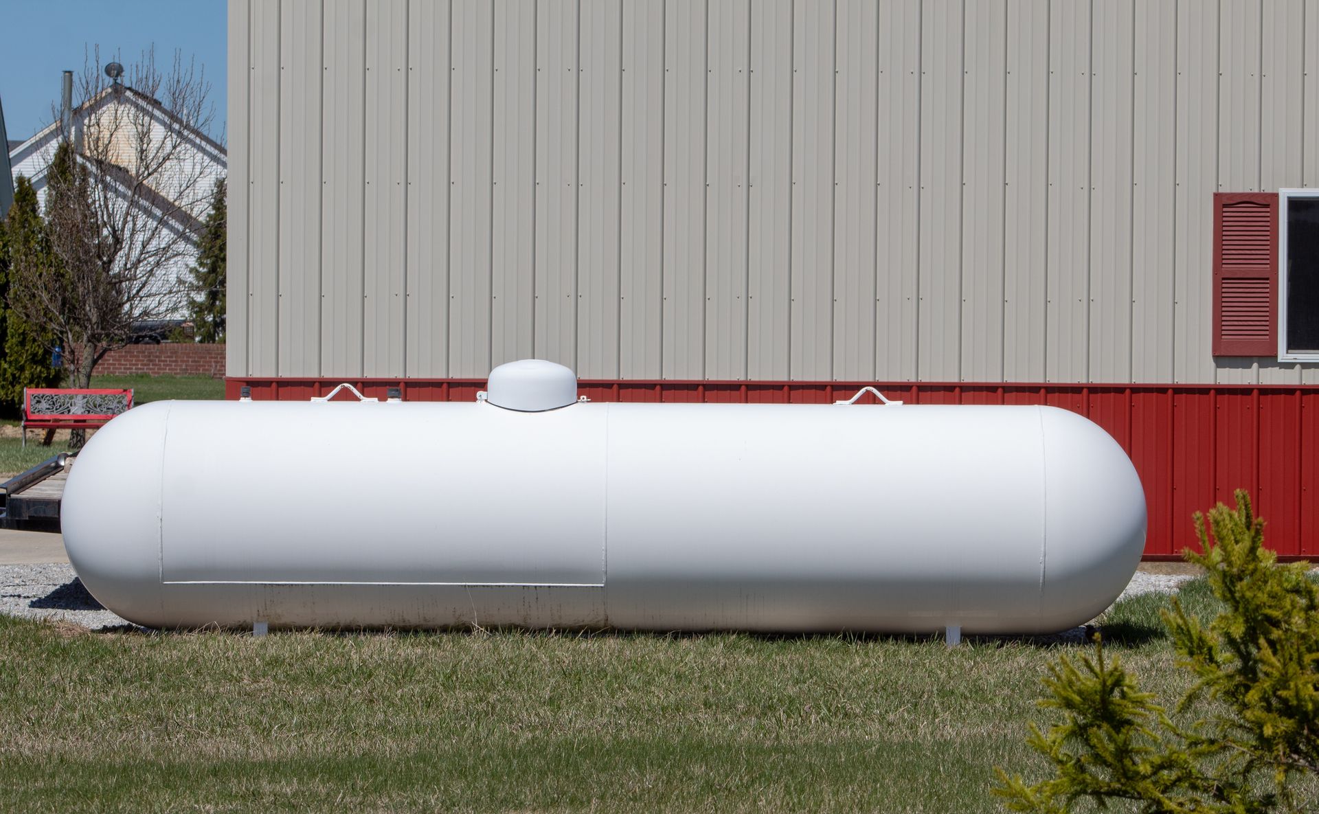 Large white propane tank beside a gray metal building with red trim Large white propane tank beside a gray metal building with red trim