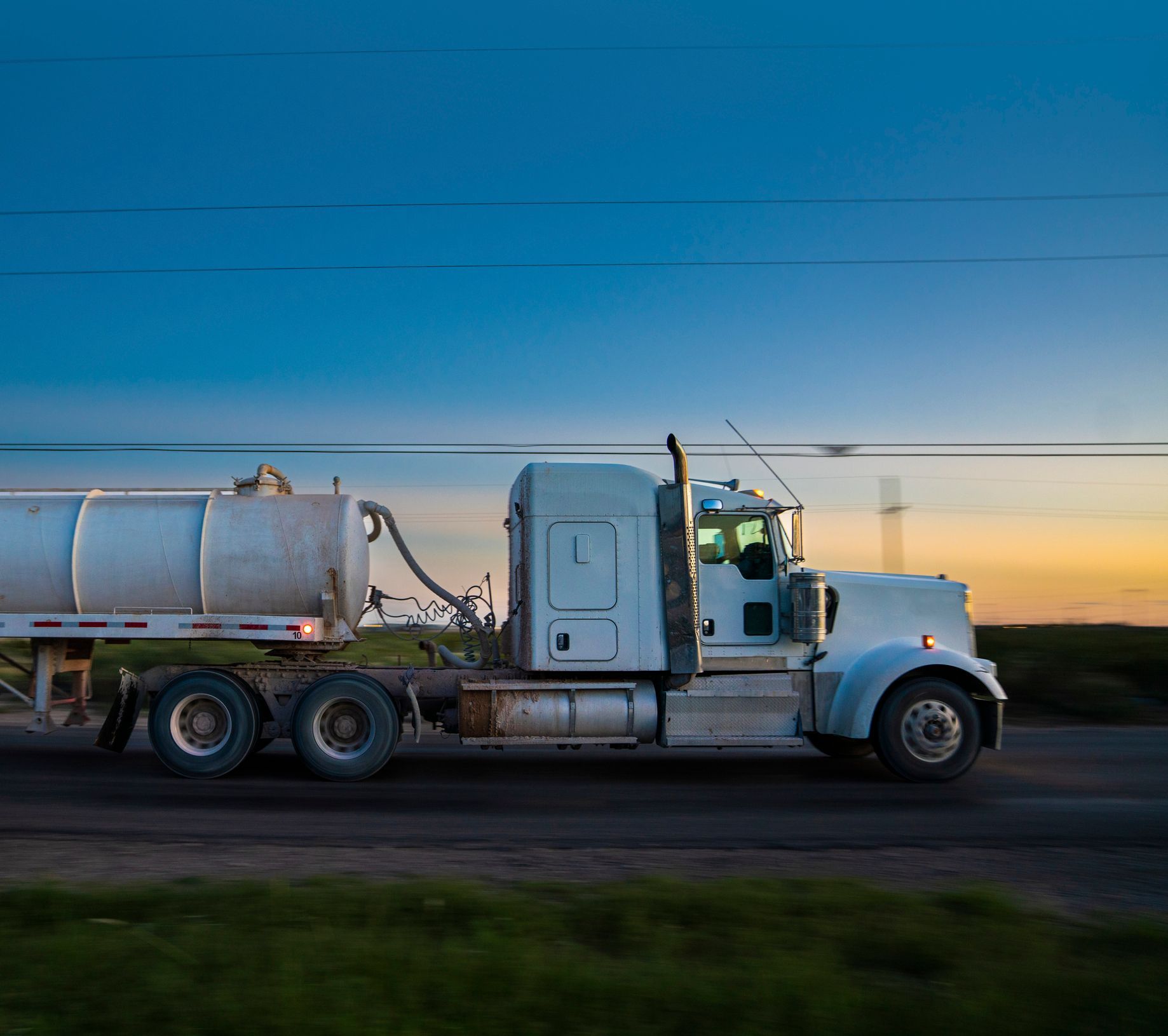 White tanker truck driving on road at dusk with clear sky. White tanker truck driving on road at dusk with clear sky.