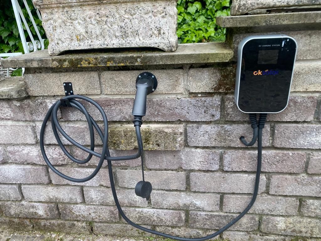 Caricabatterie per veicoli elettrici nero a parete con cavo a spirale, installato su un muro di mattoni all'aperto.