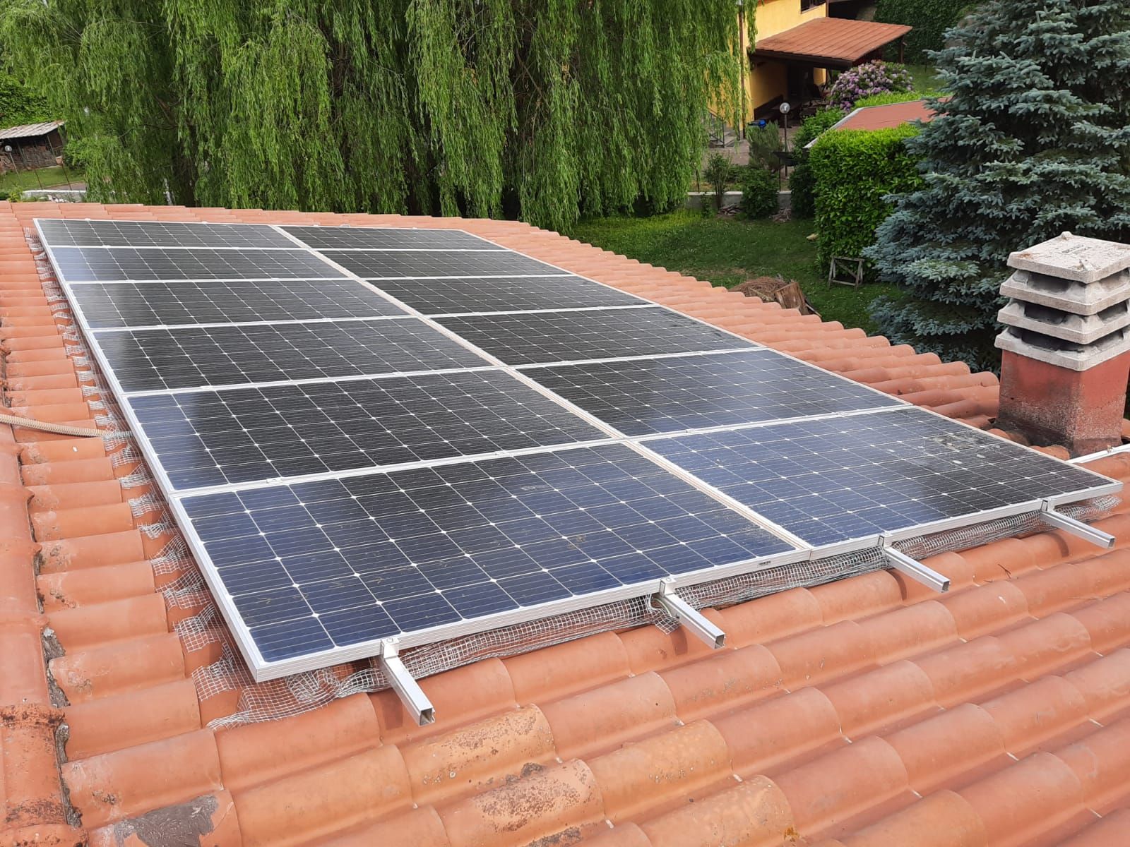 Pannelli solari installati su un tetto di tegole rosse, circondato dal verde.
