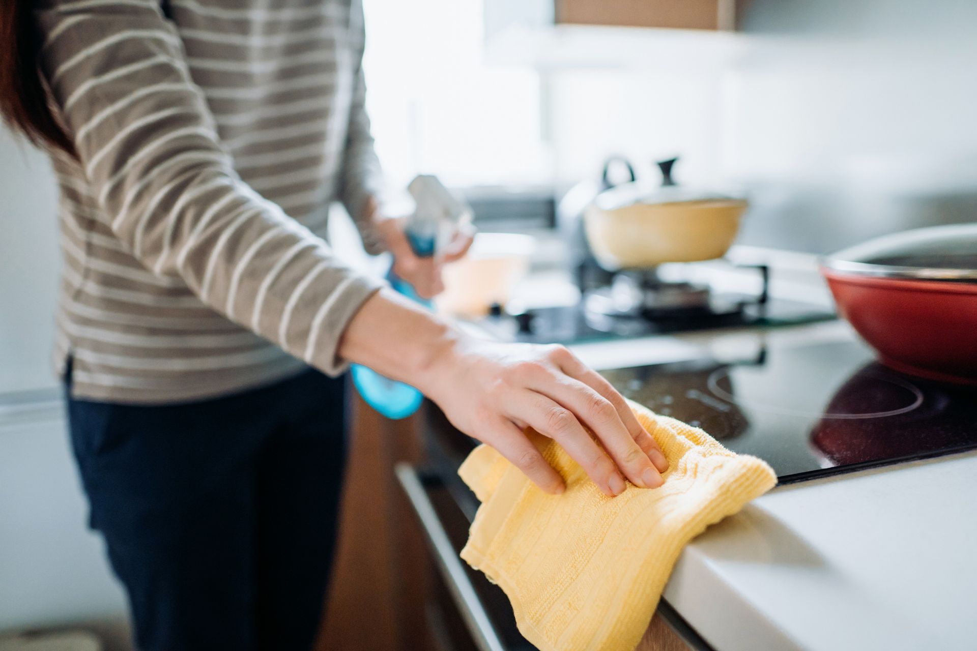 A woman is cleaning a kitchen counter with a yellow cloth. A woman is cleaning a kitchen counter with a yellow cloth.