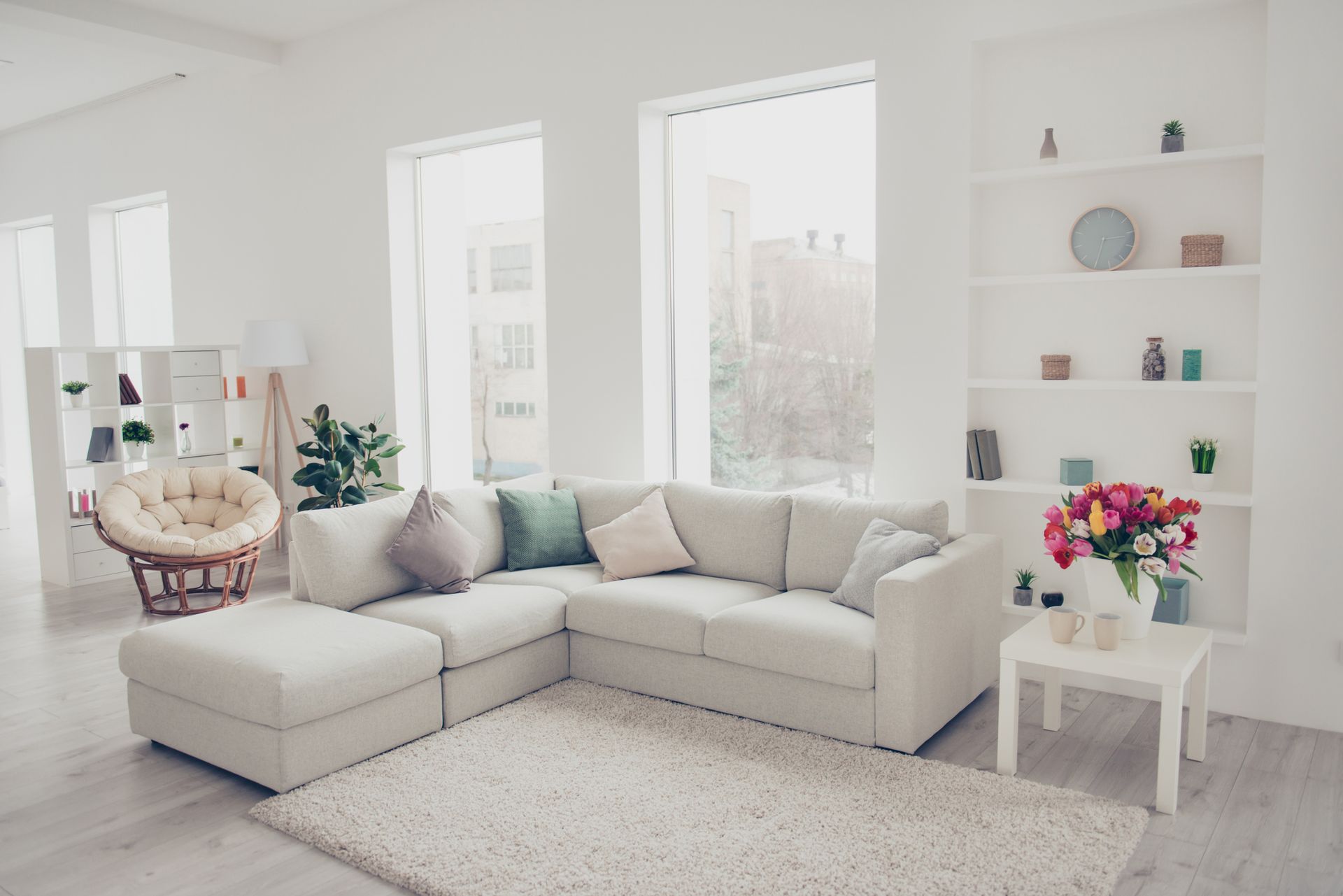 A living room with a white sectional couch , ottoman , table and chairs.