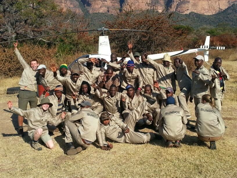 Group of hikers in beige uniforms posing outdoors with raised arms in a rocky desert setting