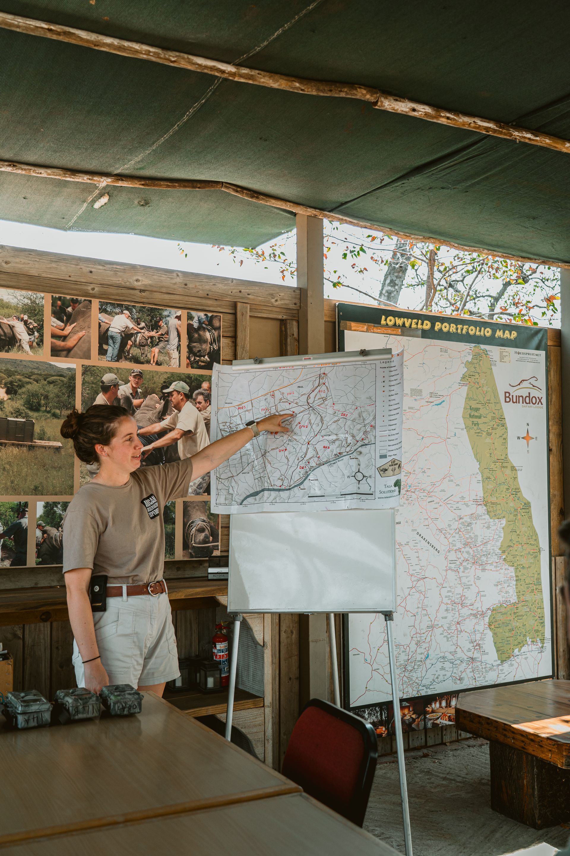 Woman points to a map on a whiteboard, explaining it to an unseen audience outdoors.