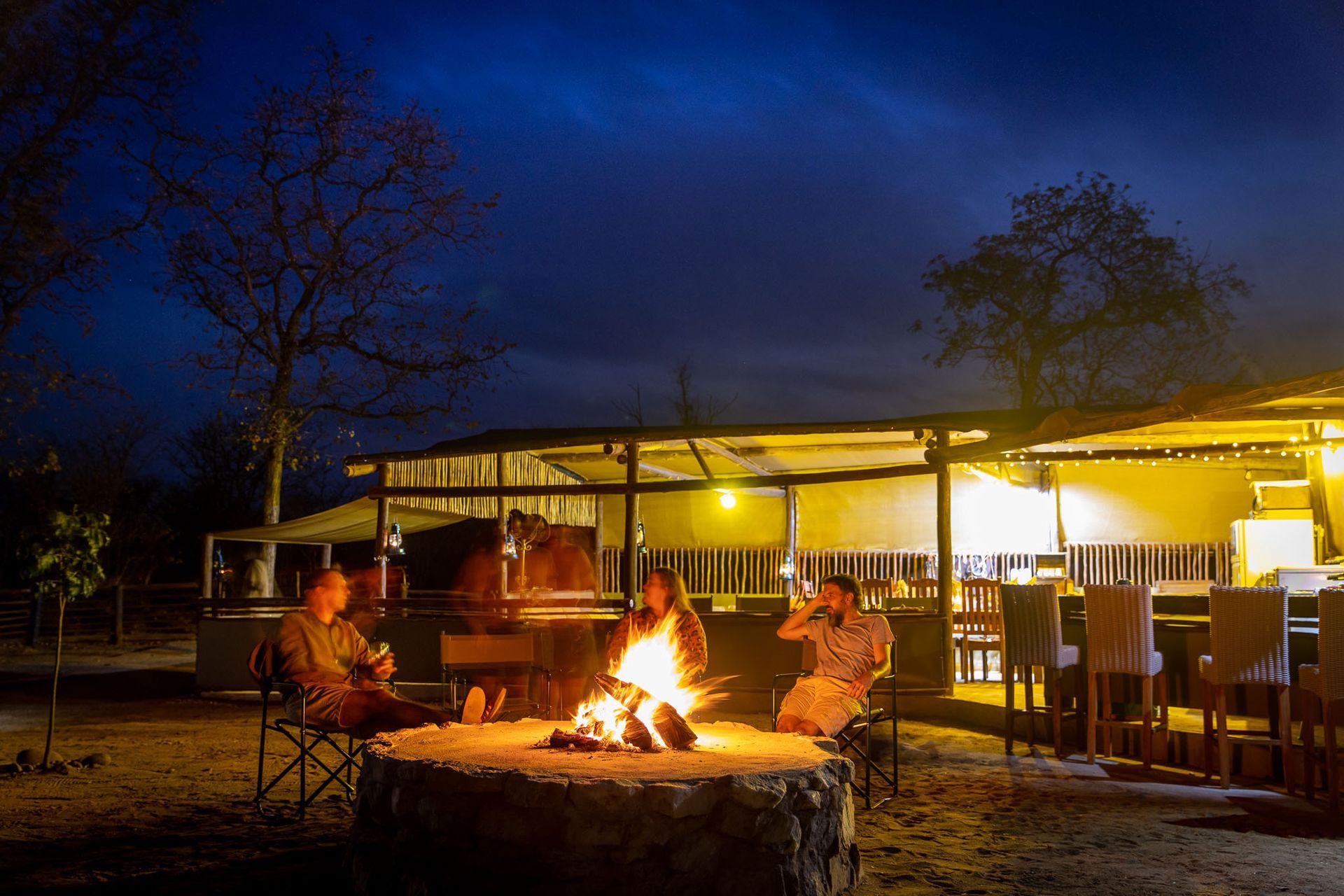 People sitting around a campfire at a lit outdoor pavilion at night