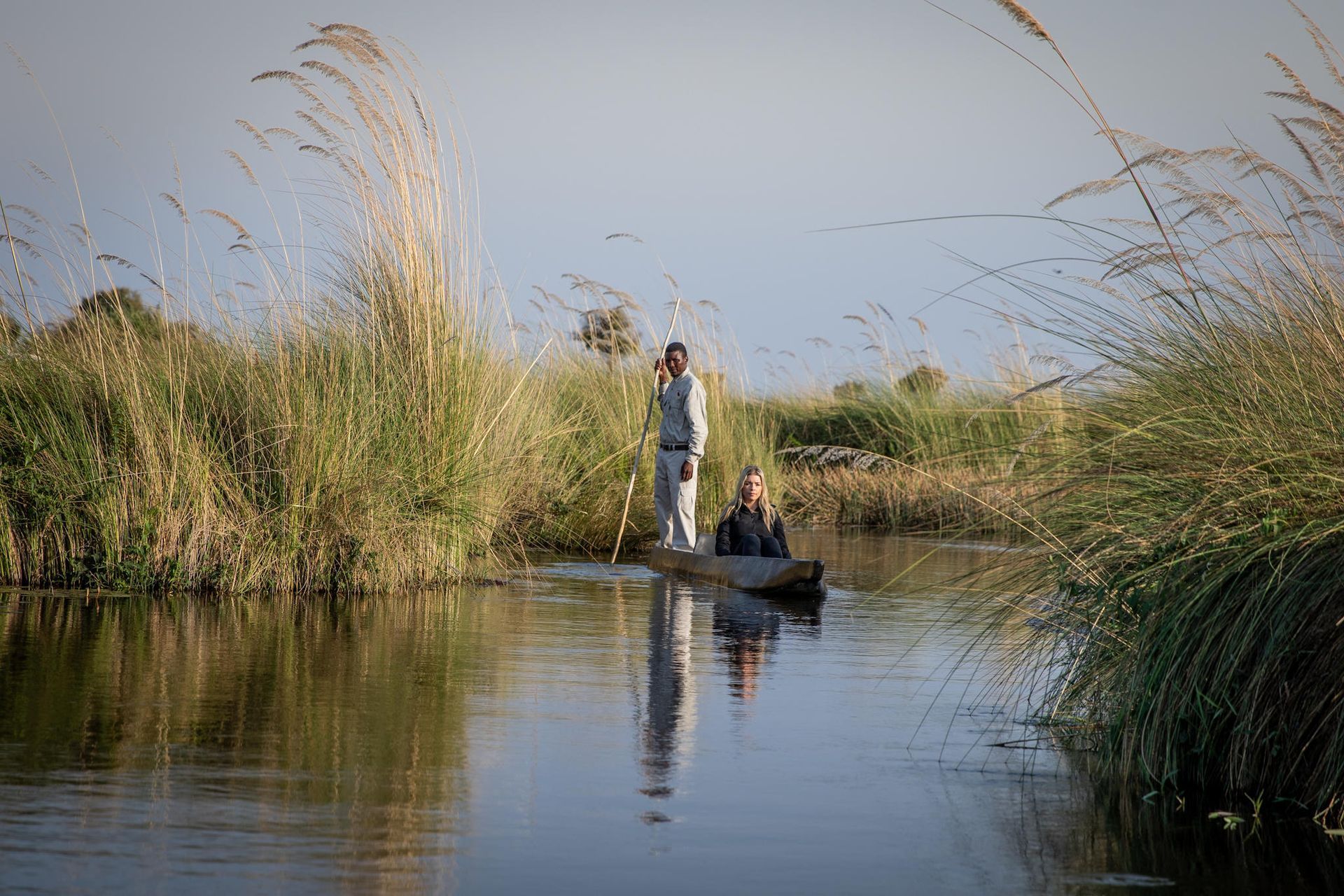 Person standing in a small boat among tall reeds on a calm river at sunset