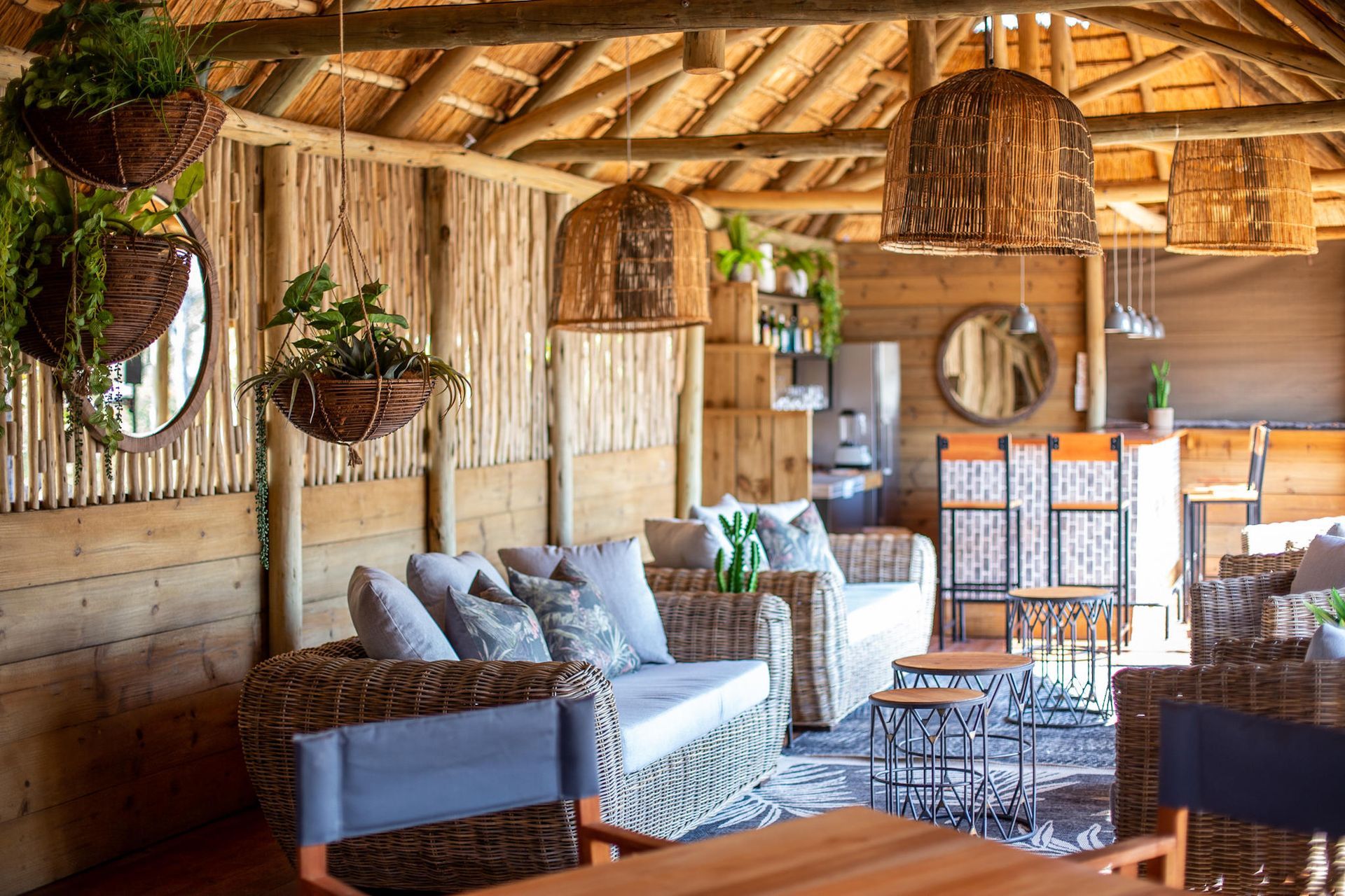 Cozy rustic lounge with wicker furniture, hanging plants, and thatched wood beams