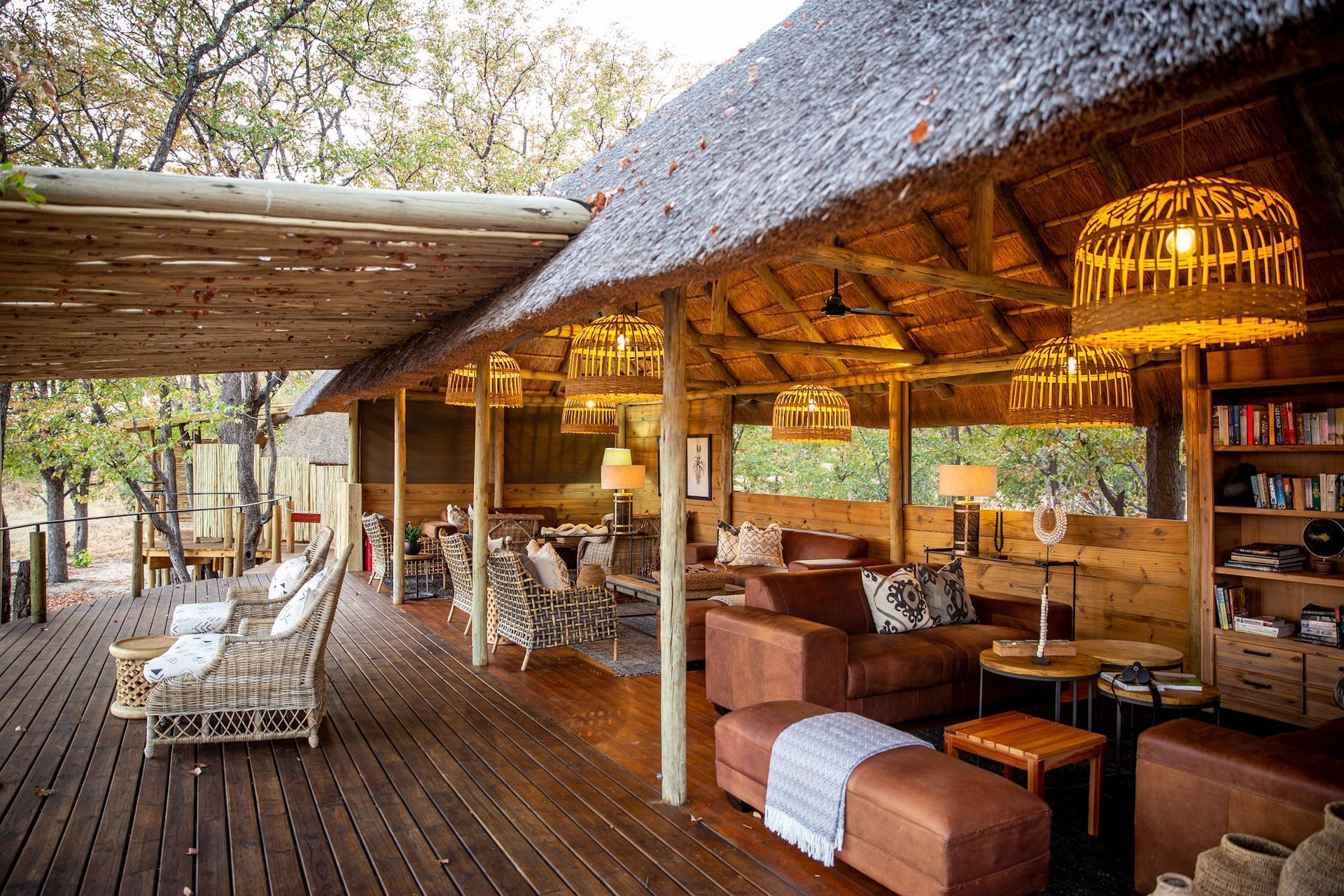 Open-air thatched lounge with wooden deck, woven chairs, warm lights, and a tropical garden view