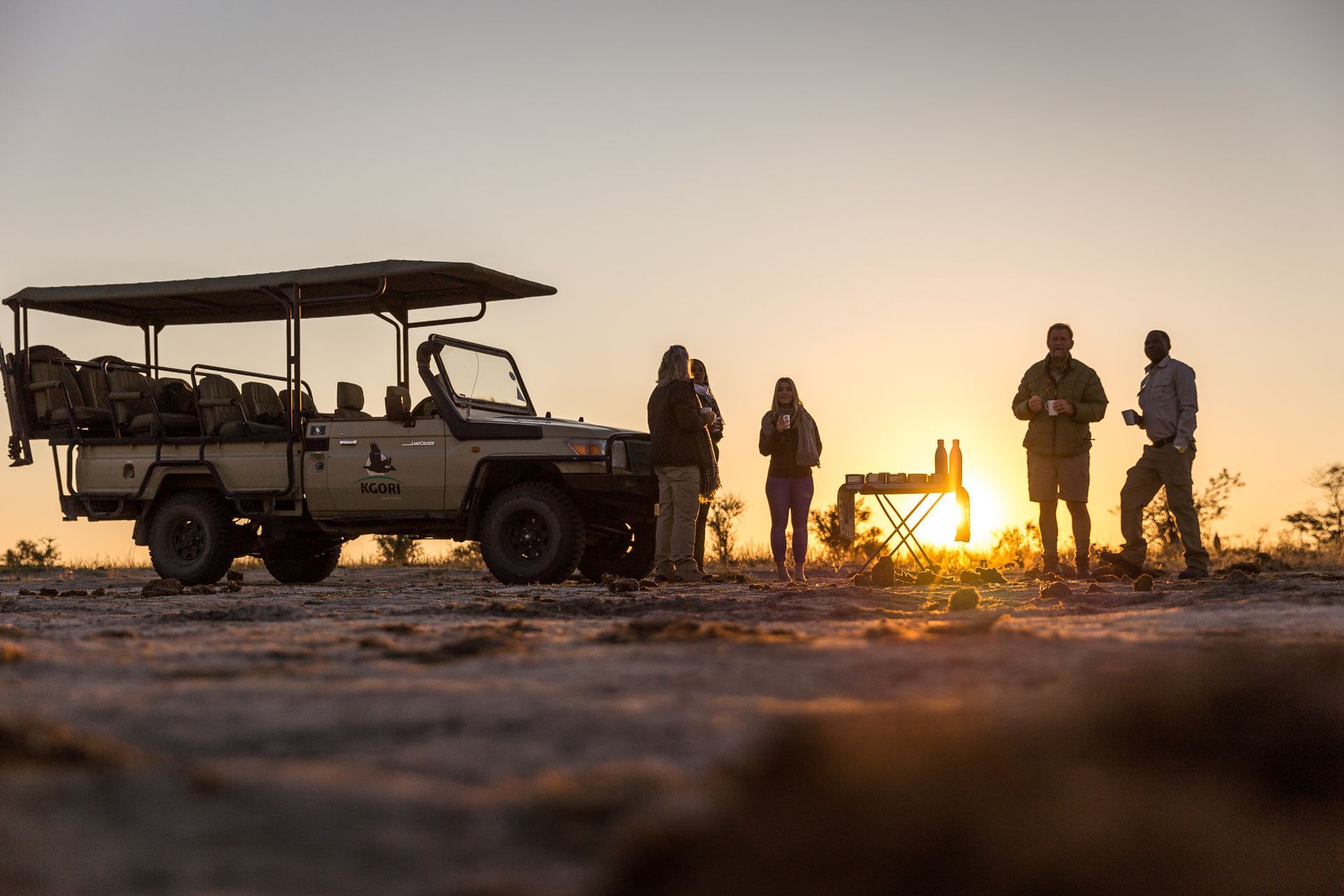 Safari jeep parked at sunset with people standing nearby.