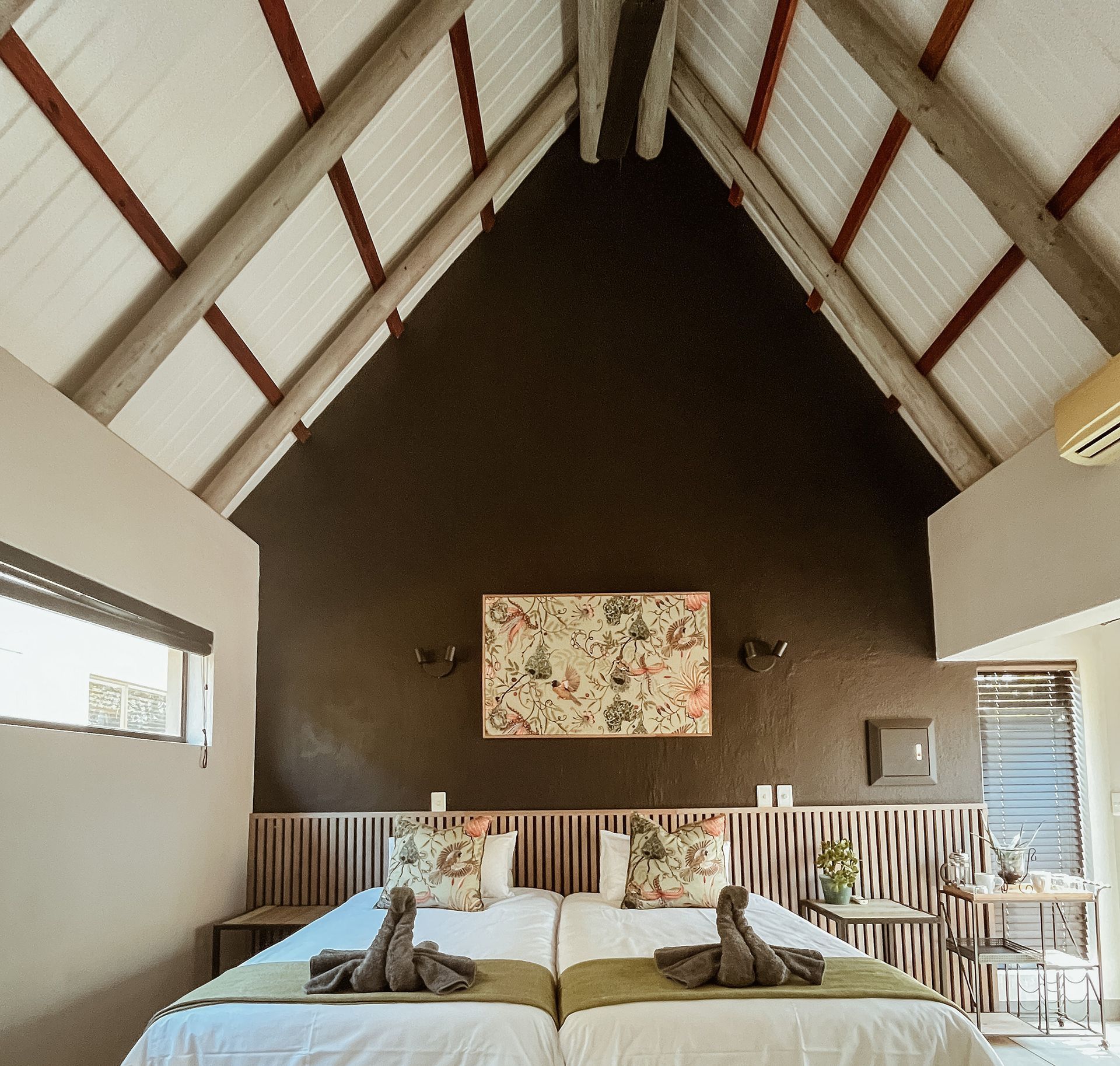 Cozy loft bedroom with vaulted ceiling, two twin beds, floral wall art, and large windows