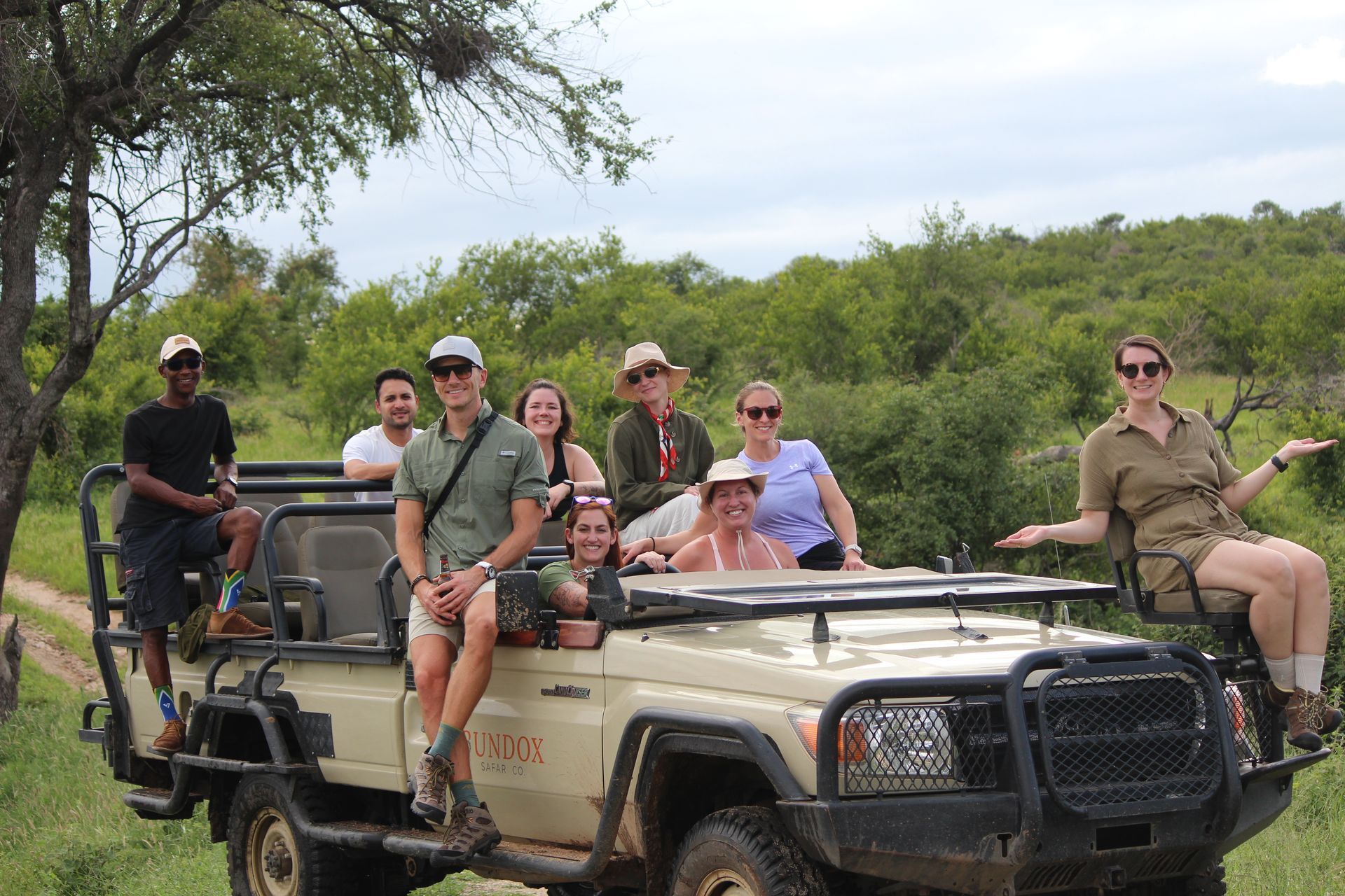 People riding in open safari vehicles on a dirt road in a green wildlife reserve.