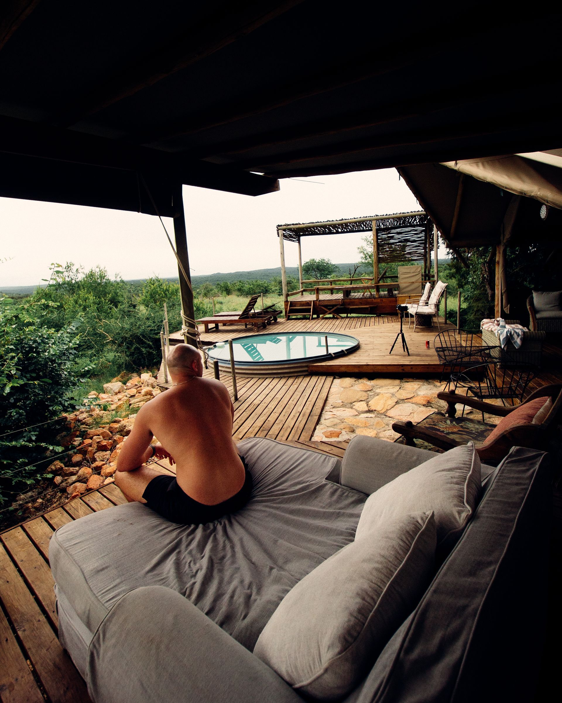 Person relaxing on an outdoor deck with sofa and hot tub, overlooking lush greenery at sunset