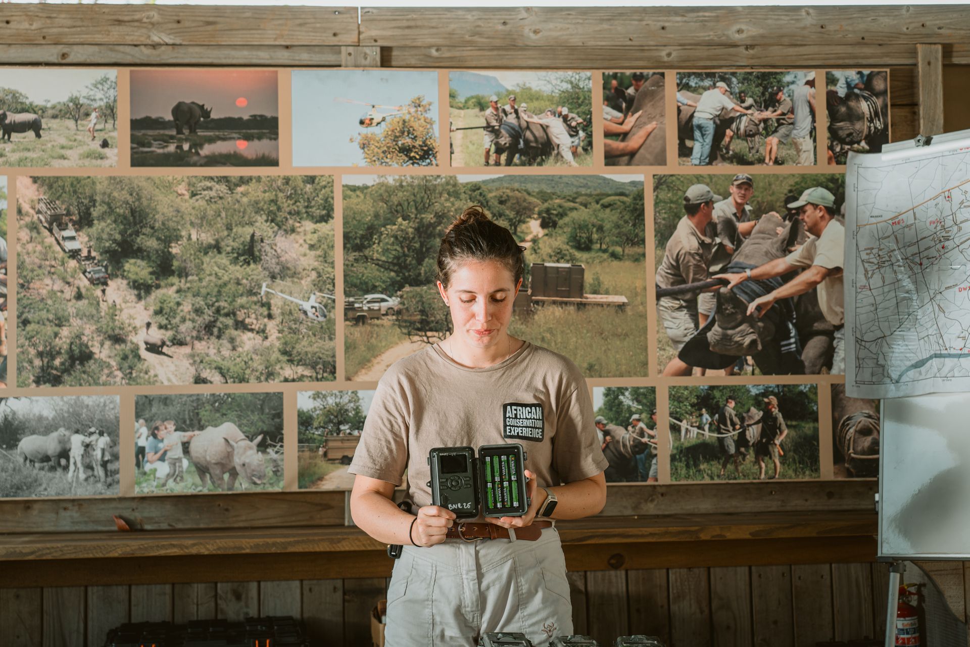 Person holding a tablet in front of a wall of outdoor photos and maps in a rustic room