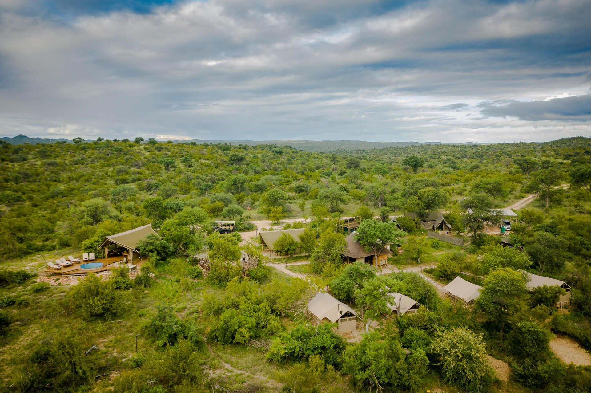 Aerial view of a lush green forest village with scattered huts under a cloudy sky
