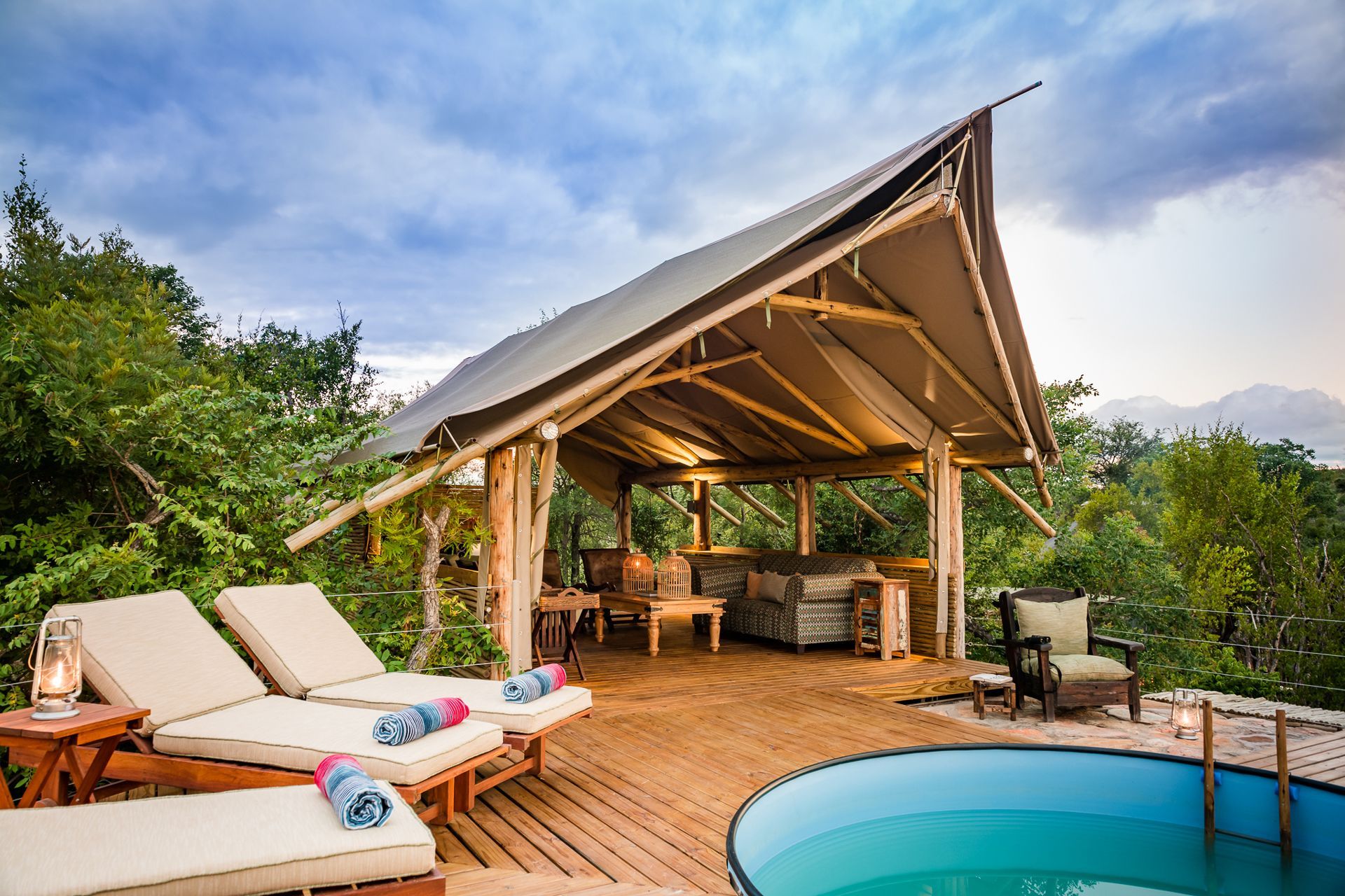 Tropical resort deck with lounge chairs, thatched cabana, and small blue pool at sunset