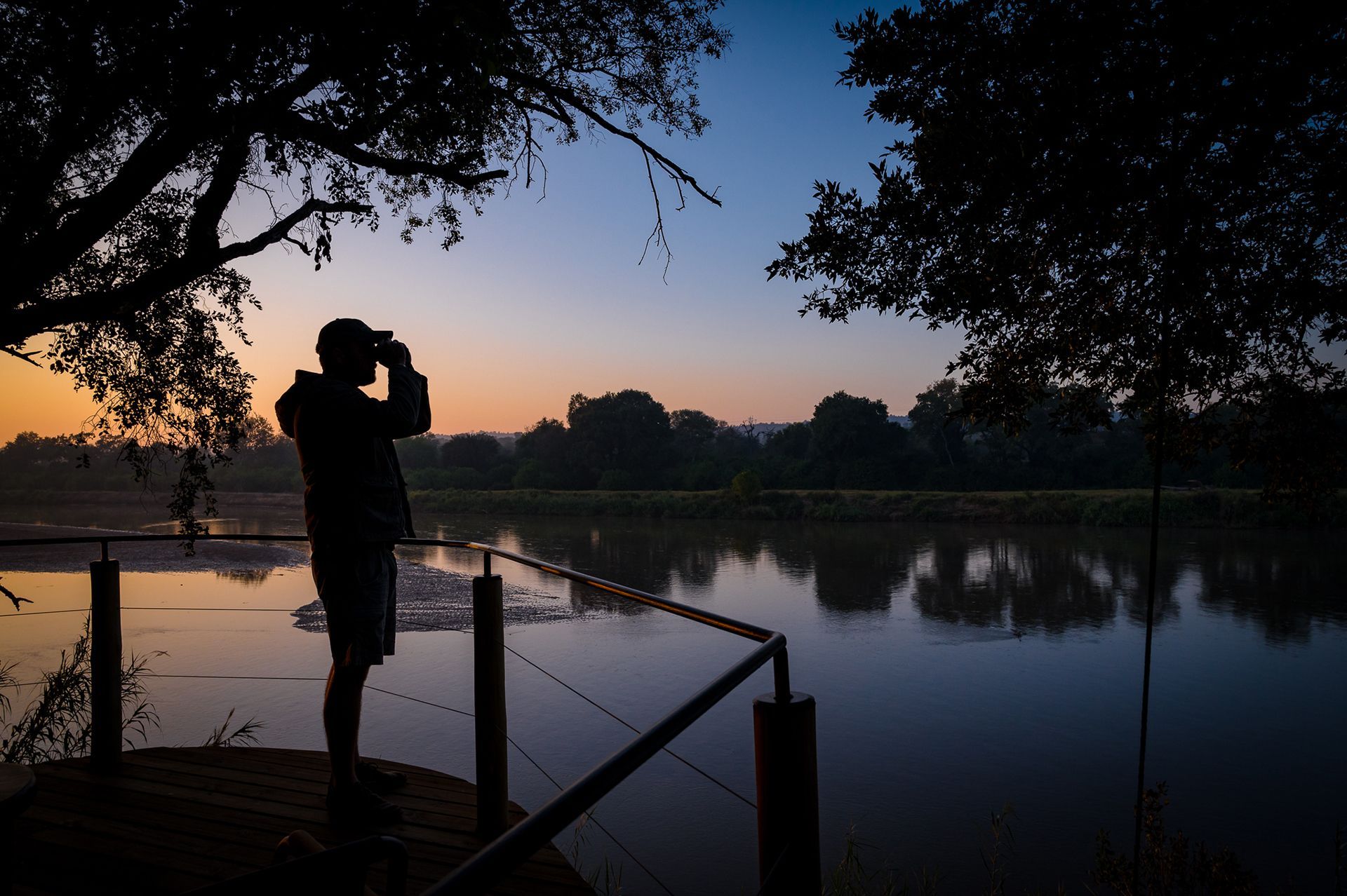 Silhouette of a person photographing a sunrise over a calm lake from a dock