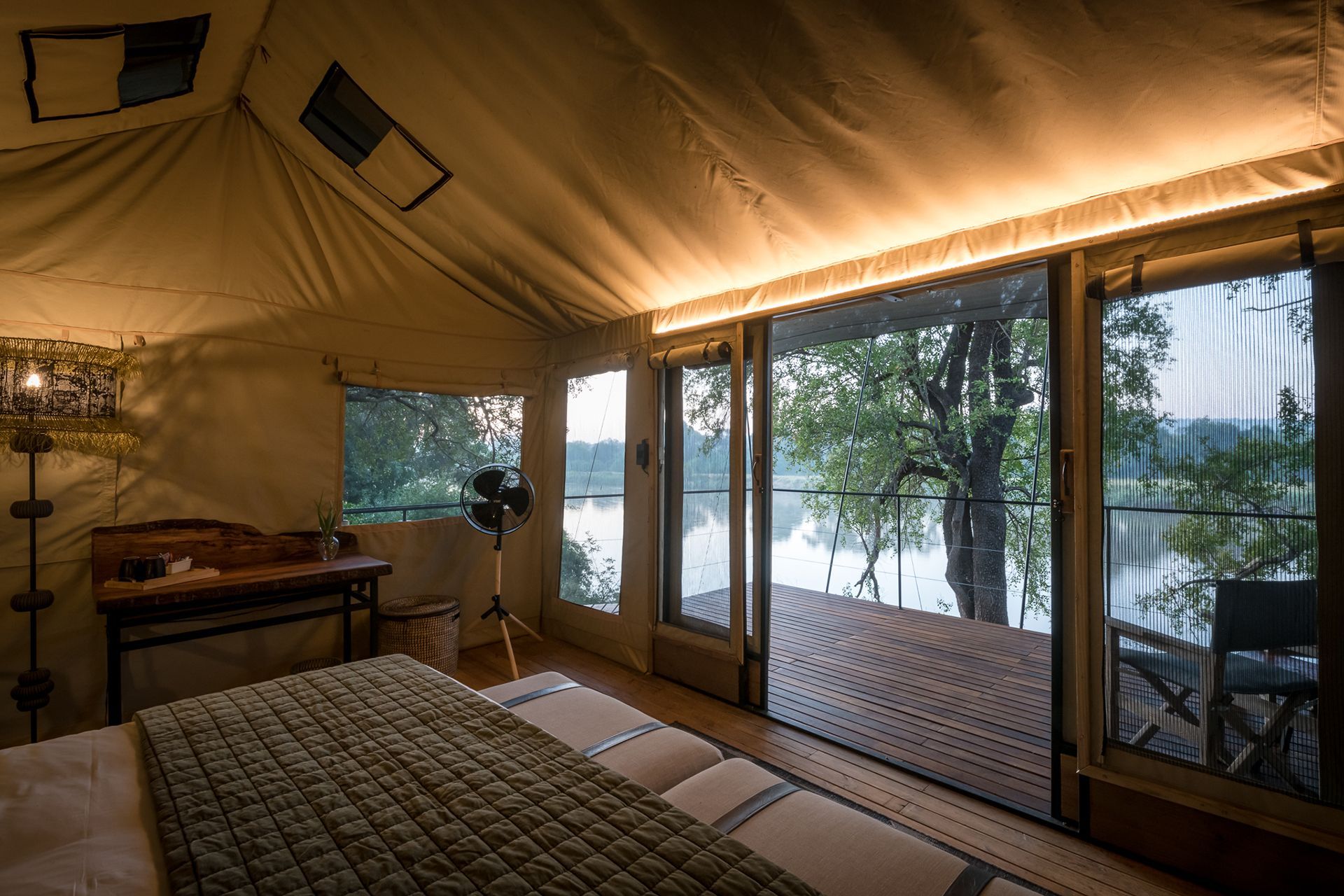 Inside of a glamping tent with a bed, desk, and large open doors with a view of the Olifant River