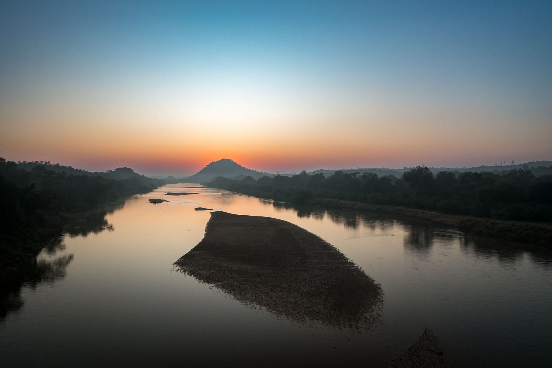 Sunrise over a river and forested banks, with a small island in the water; orange and blue sky.