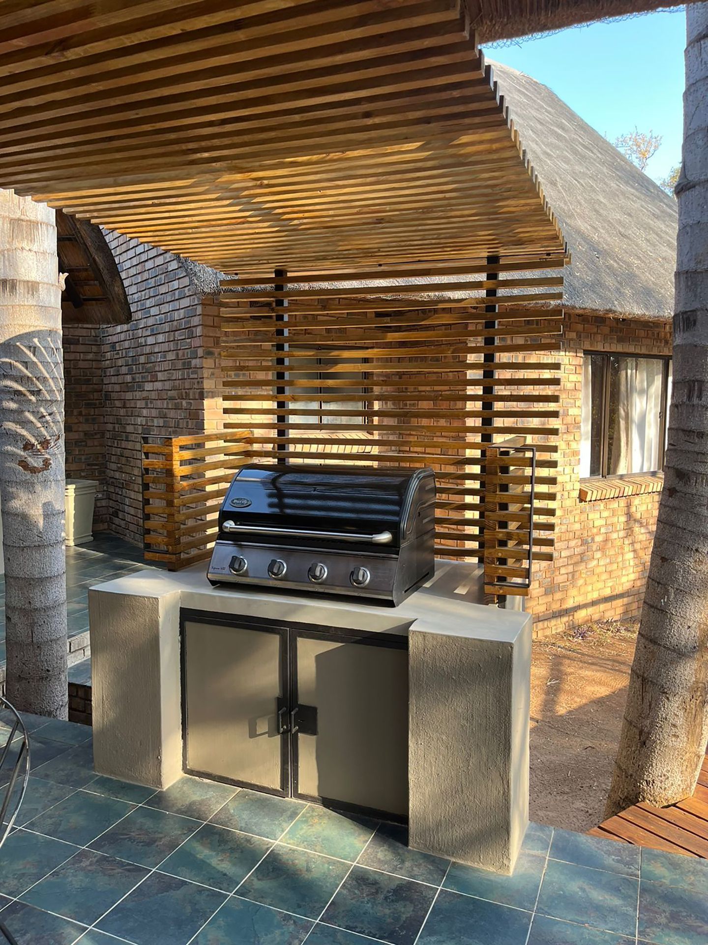 Outdoor grilling station with a built-in grill, wooden accents, and stone counter, next to a brick building.