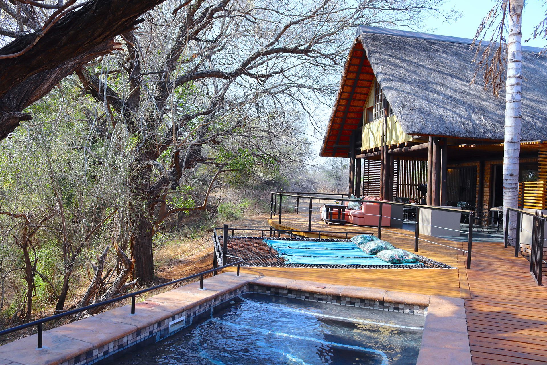 Lodge deck with a plunge pool beside trees, overlooking a dry riverbed in bright daylight