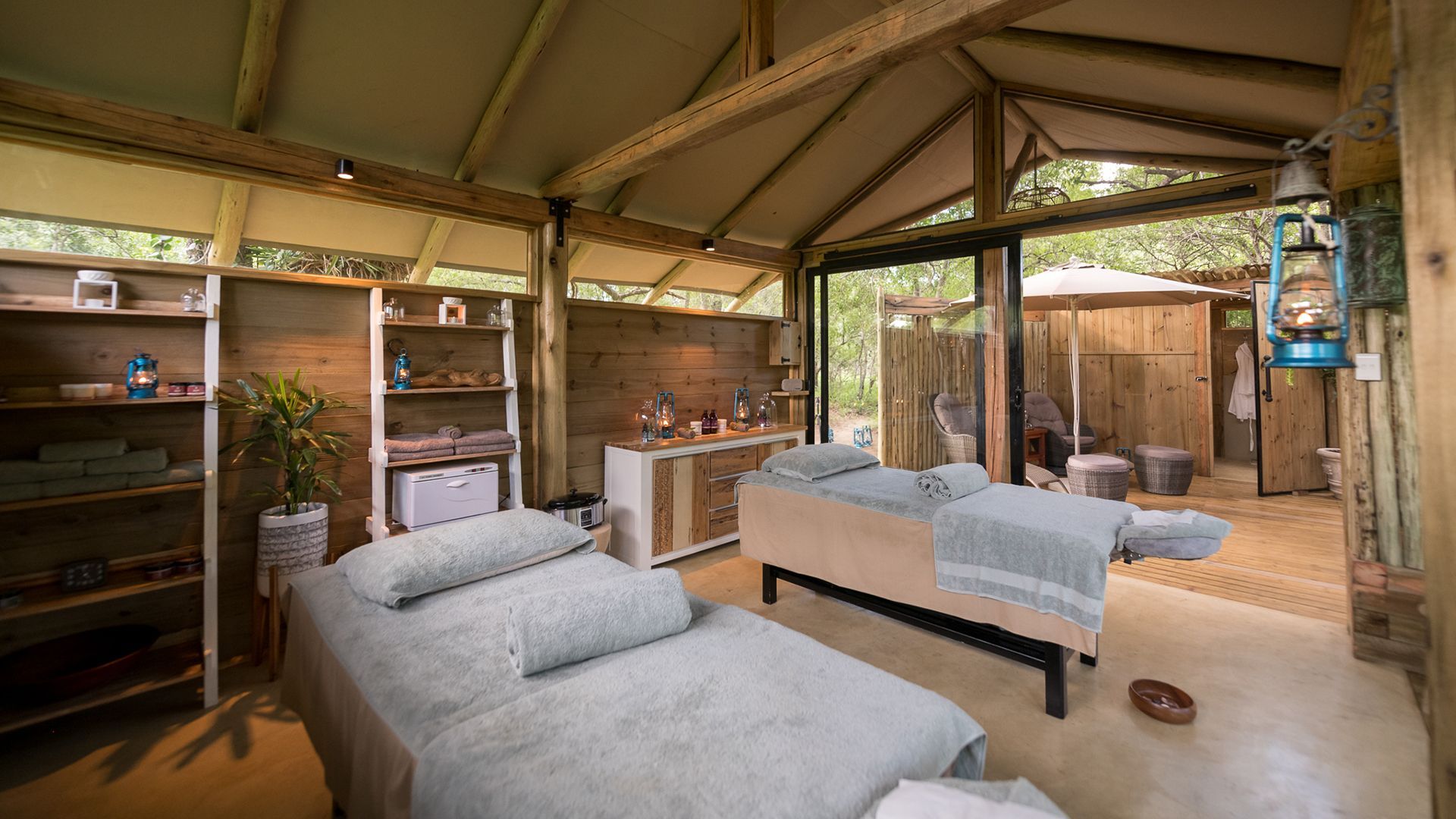 Spa treatment room with two massage tables, light wood, and open to an outdoor area.