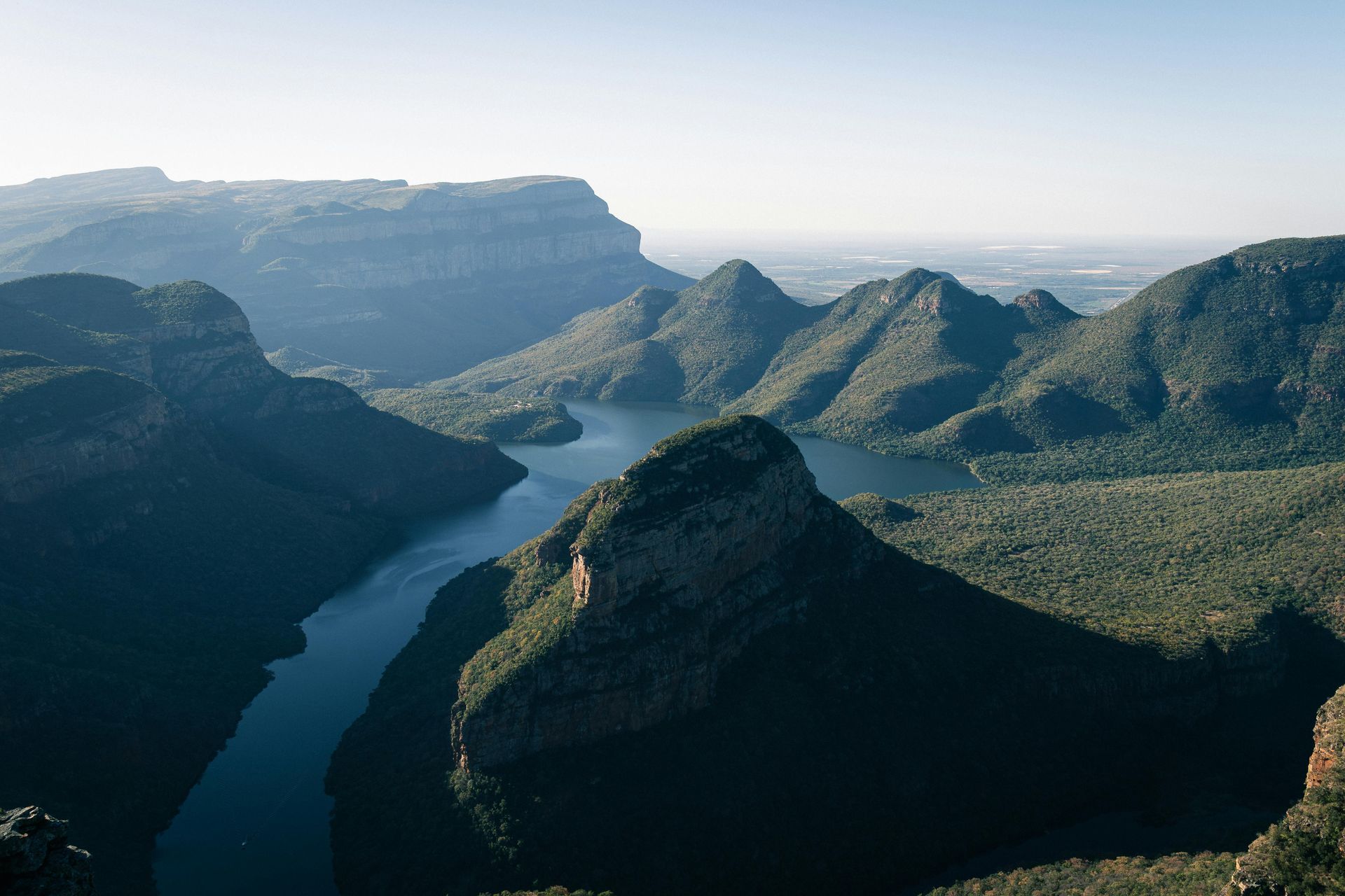 A winding river cuts through green mountains and steep cliffs under a clear sky.