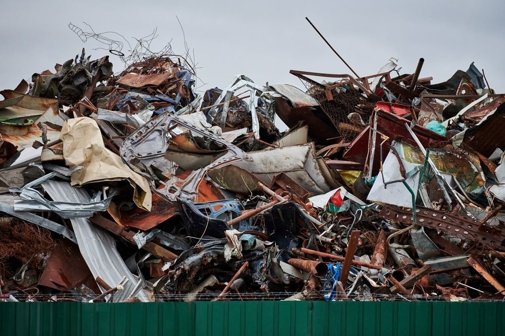 A Pile of Scrap Metal Is Sitting in Front of A Green Fence — H & H Metal Recycling In Noosa, QLD