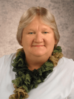 Studio portrait of a smiling person in a white top with a green ruffled scarf against a beige backdrop