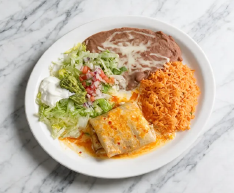Plate with refried beans, rice, enchiladas, and lettuce salad on a marble table
