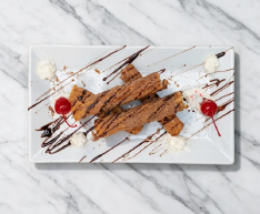 Chocolate dessert on a white plate with whipped cream, strawberry sauce, and chocolate drizzle on marble surface