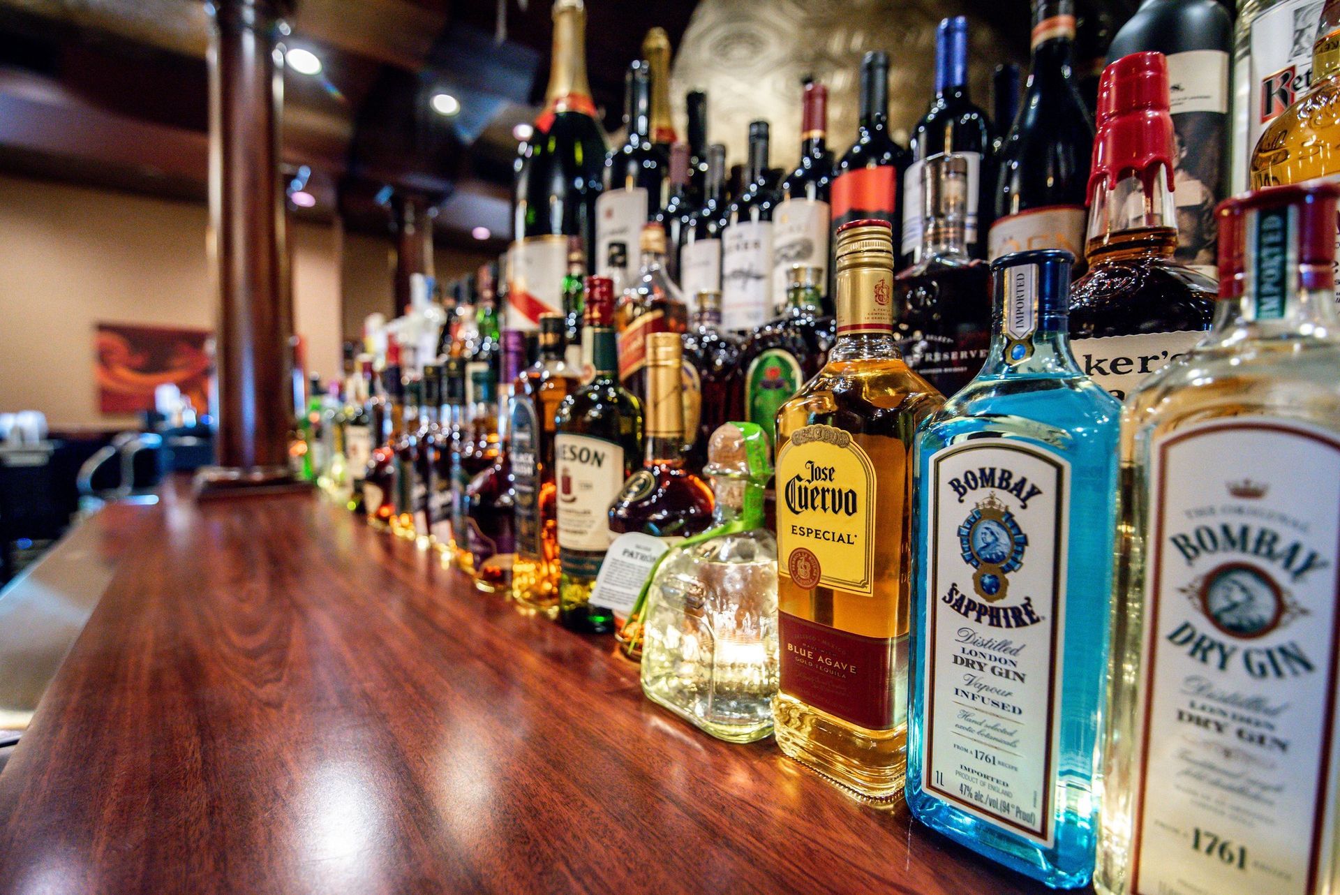 Row of liquor bottles on a polished bar counter in a dimly lit bar