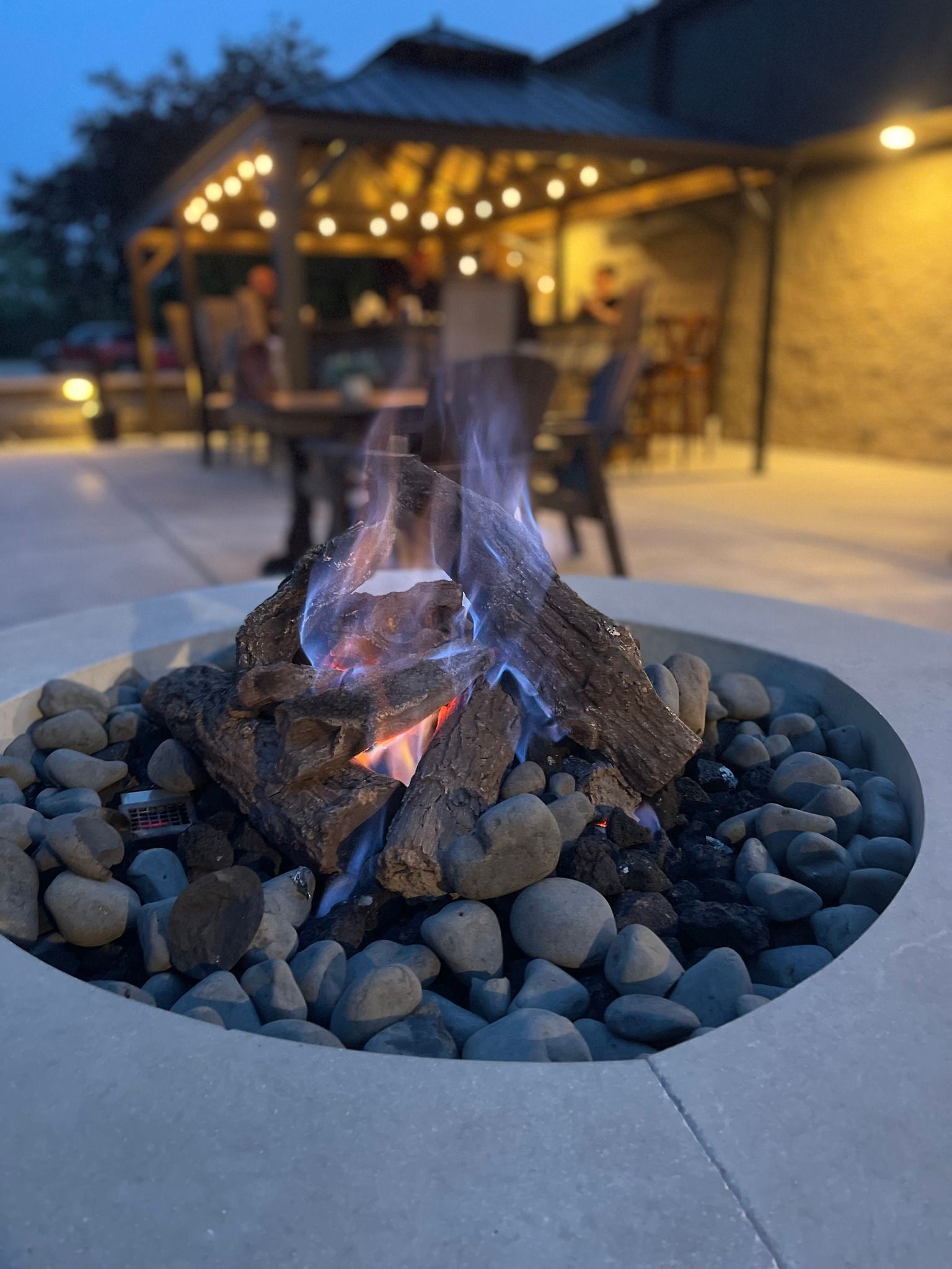 Backyard fire pit with glowing embers and string lights on a patio at dusk