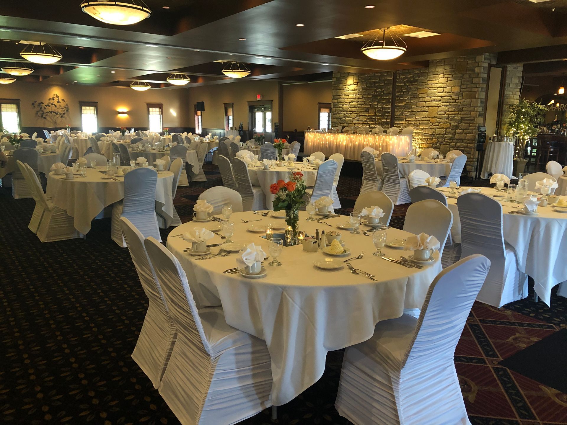 Banquet hall with round tables set for a formal event, covered in white tablecloths and chair covers.