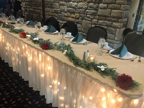 Decorated banquet table with fairy lights, greenery, and folded napkins against a stone wall