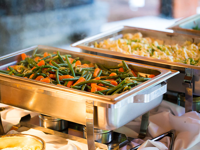 Buffet trays of mixed vegetables and rice on a stainless-steel serving line