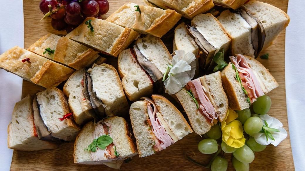 Assorted sandwich platter on a wooden board with grapes and cheese cubes