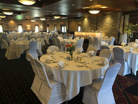 Formal banquet hall with round, white-clothed tables and chair covers set for an event