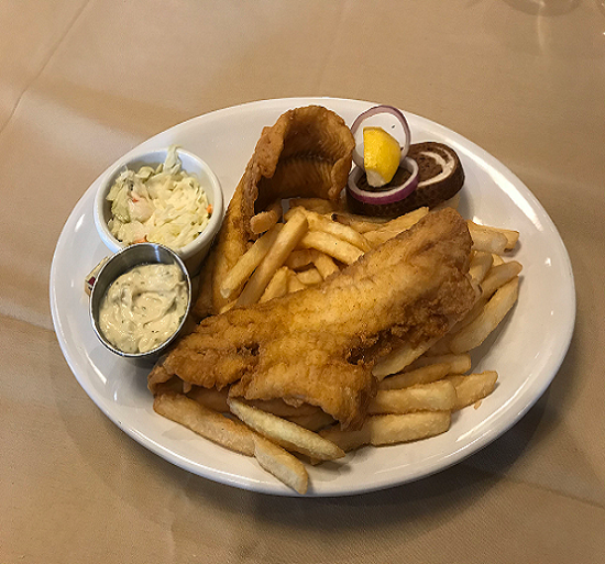 Plate of fried fish and French fries with coleslaw, tartar sauce, and lemon wedges on a table
