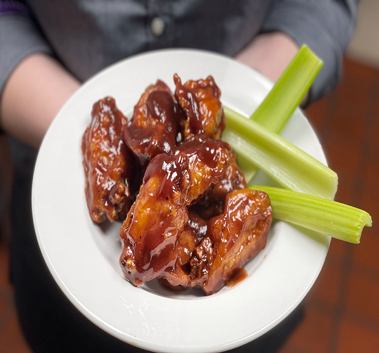 Glazed chicken wings on a white plate with celery sticks