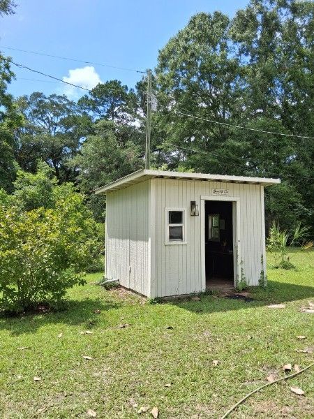 Small white shed with an open door in a grassy yard surrounded by trees under a blue sky
