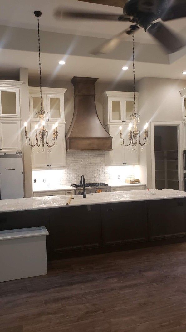Unfinished kitchen with large island, cream cabinets, and built-in appliances in a home interior.