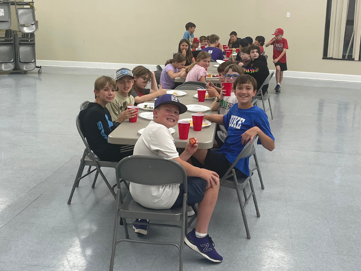 A group of children are sitting at tables with red cups and plates