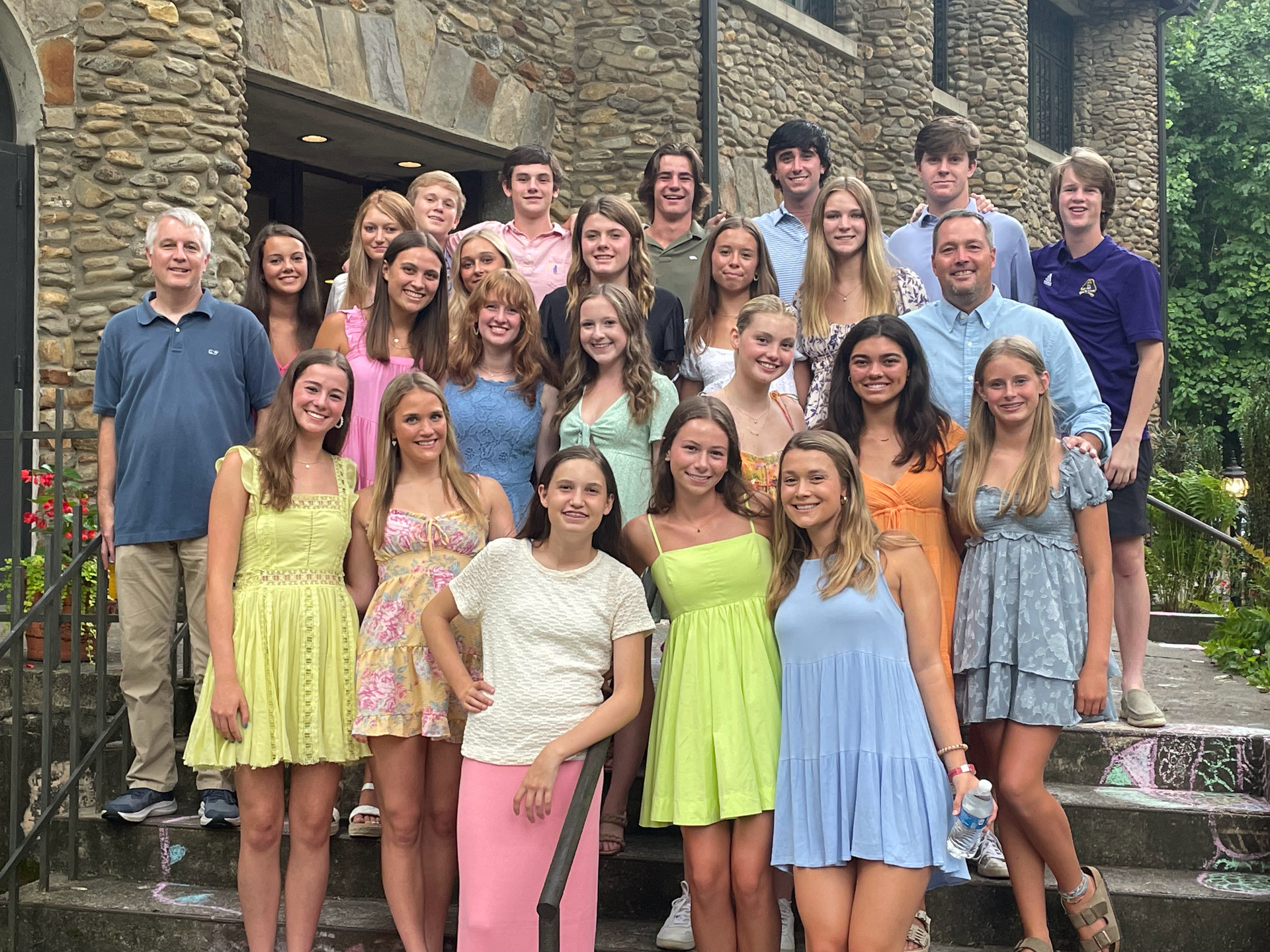 A group of young people are posing for a picture in front of a stone building.